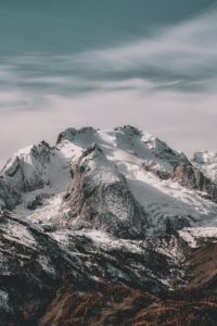 Snow-covered mountain range under cloudy sky Snowy mountain peaks with cloudy sky